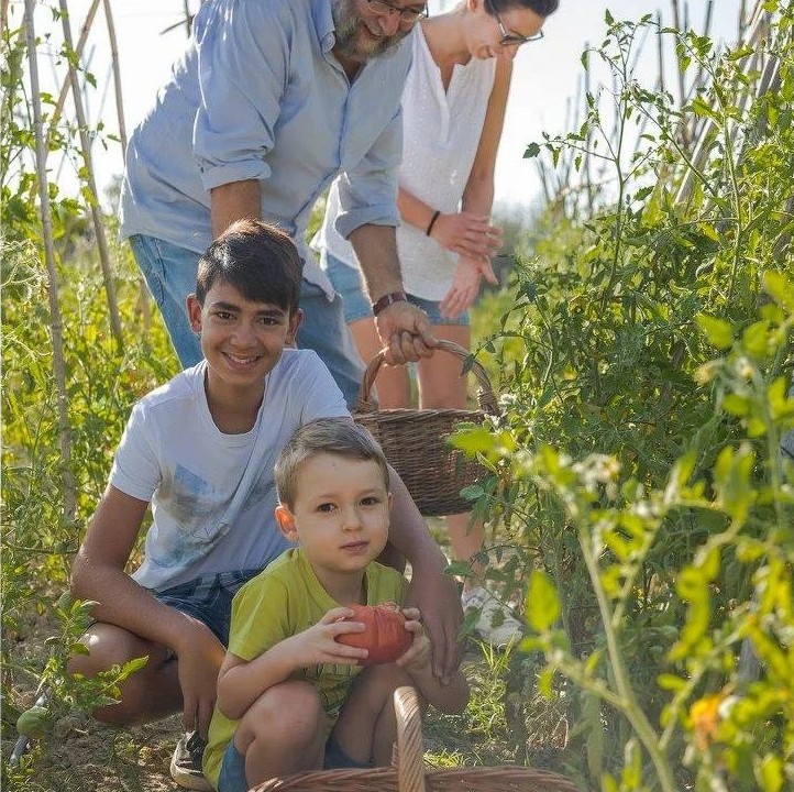 La famiglia raccoglie pomodori nell'orto del podere, con i bambini e i cesti di vimini
