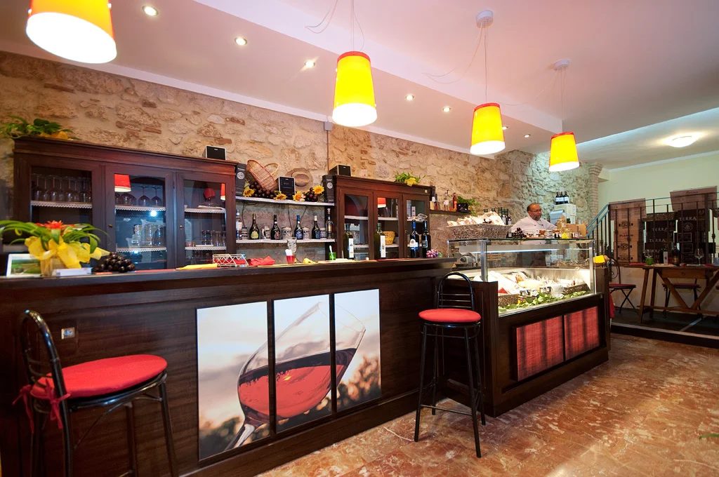 L'interno dell'enoteca: bancone, scaffali di vini e lampade colorate